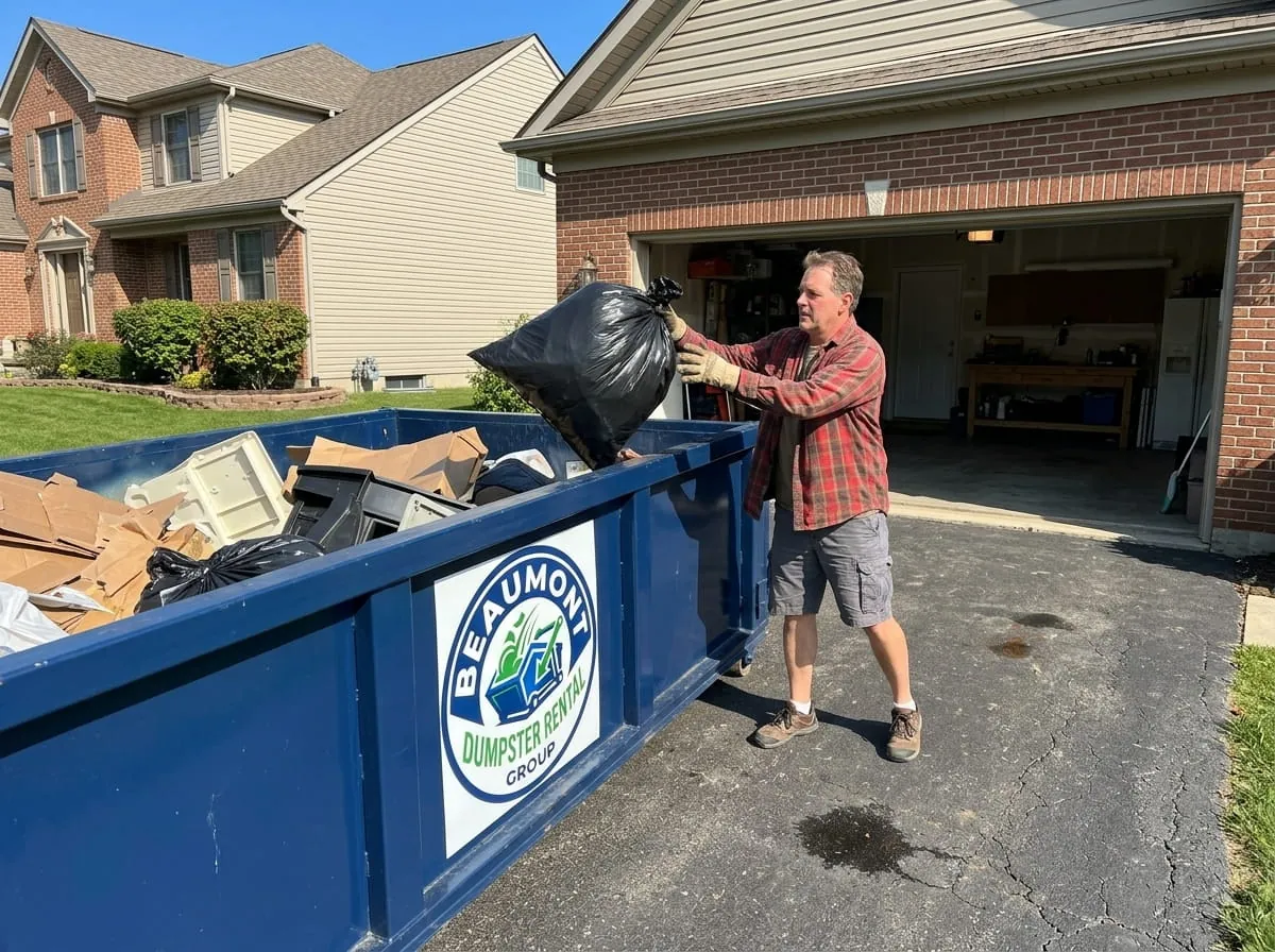Homeowner loading a bag of household junk into a roll-off dumpster in Beaumont, Texas